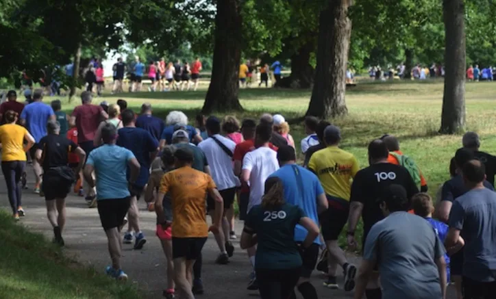 Photograph of a host of runners in sports clothing shot from behind as they run through a park area with trees
