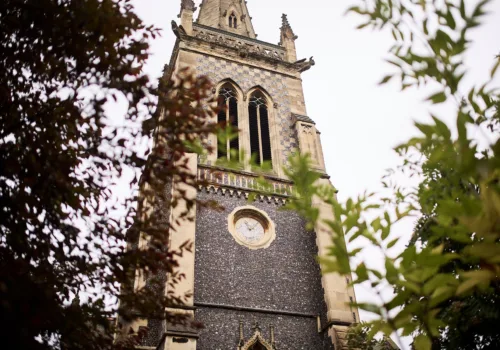 Ipswich Minster's stone church tower with clock face, seen from below through tree foliage