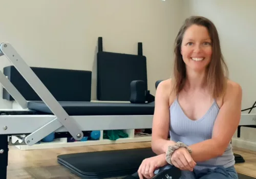 Woman in grey vest top sitting in front of some fitness equipment