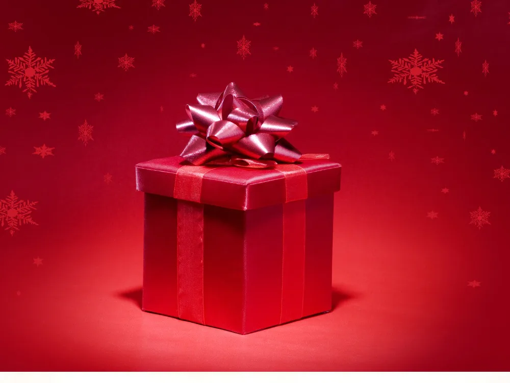 Red wrapped gift box topped with a red bow, on a red background scattered with snowflakes