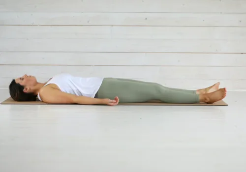 A woman lies in a yoga pose on a mat.