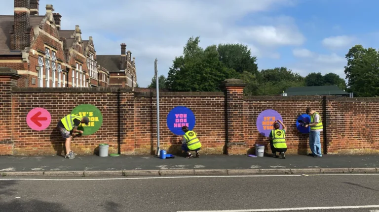Four people in hi-vix jackets painting graphics onto a brick wall in front of a large building