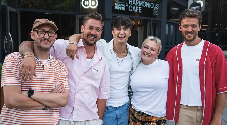 Five smiling people standing in front of a building labelled Good Supper x Harmonious Cafe