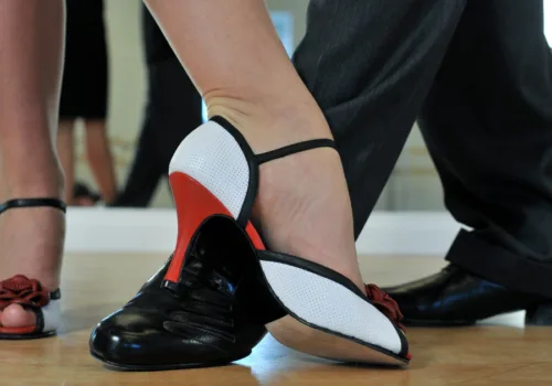 two pairs of feet - one in black, low lace-up shoes; the other in red, white and black heeled sandals both in a dance position